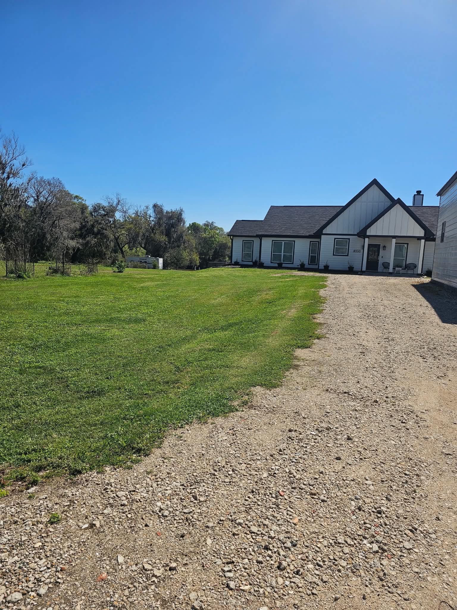 A white modern farmhouse with black trim behind a freshly mown front lawn, gravel drive running up to the porch