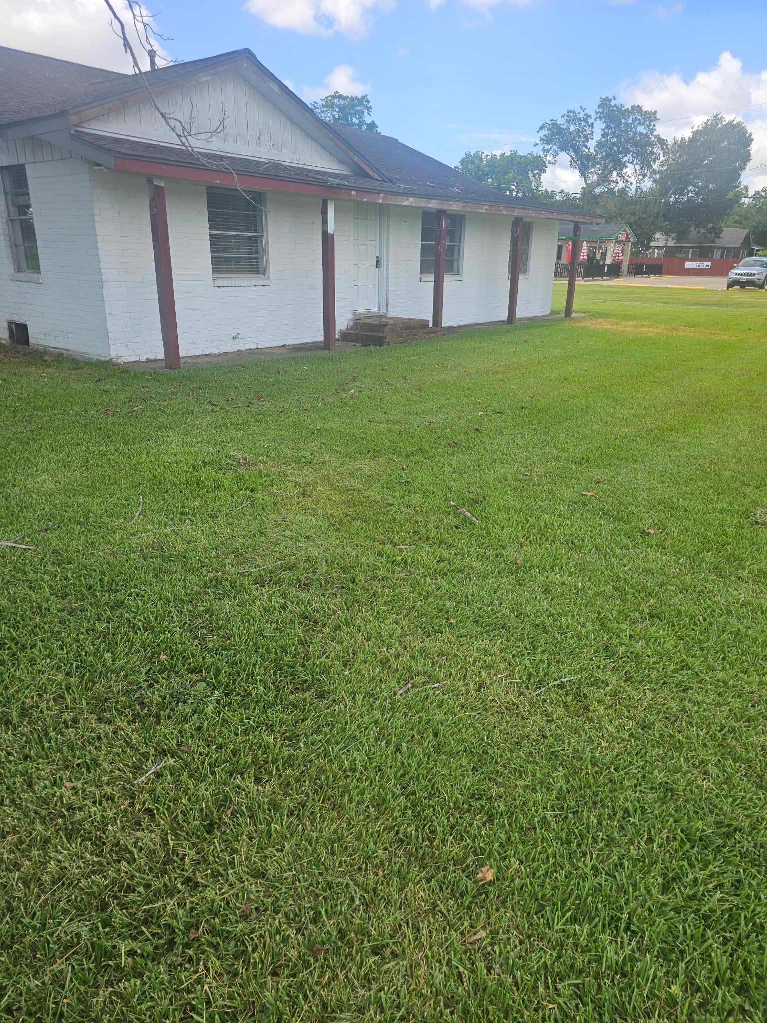A white painted-brick house with maroon porch posts, the lawn cut right up to the slab